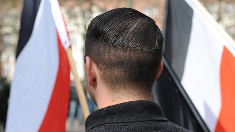 Ein Mann steht mit einer Nazi-Flagge bei einer Kundgebung.
